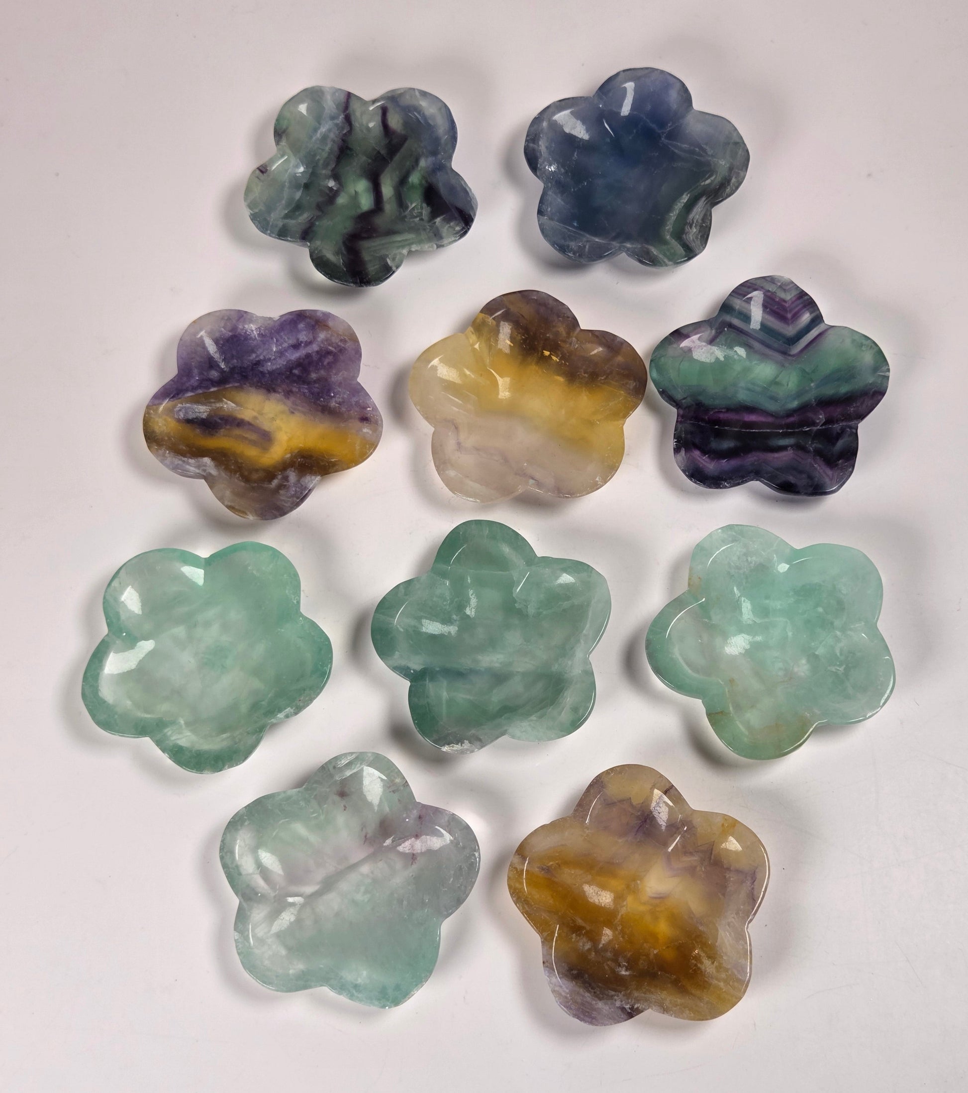 Nine carved gemstone flower-shaped bowls in various colors and patterns, arranged on a plain white background.