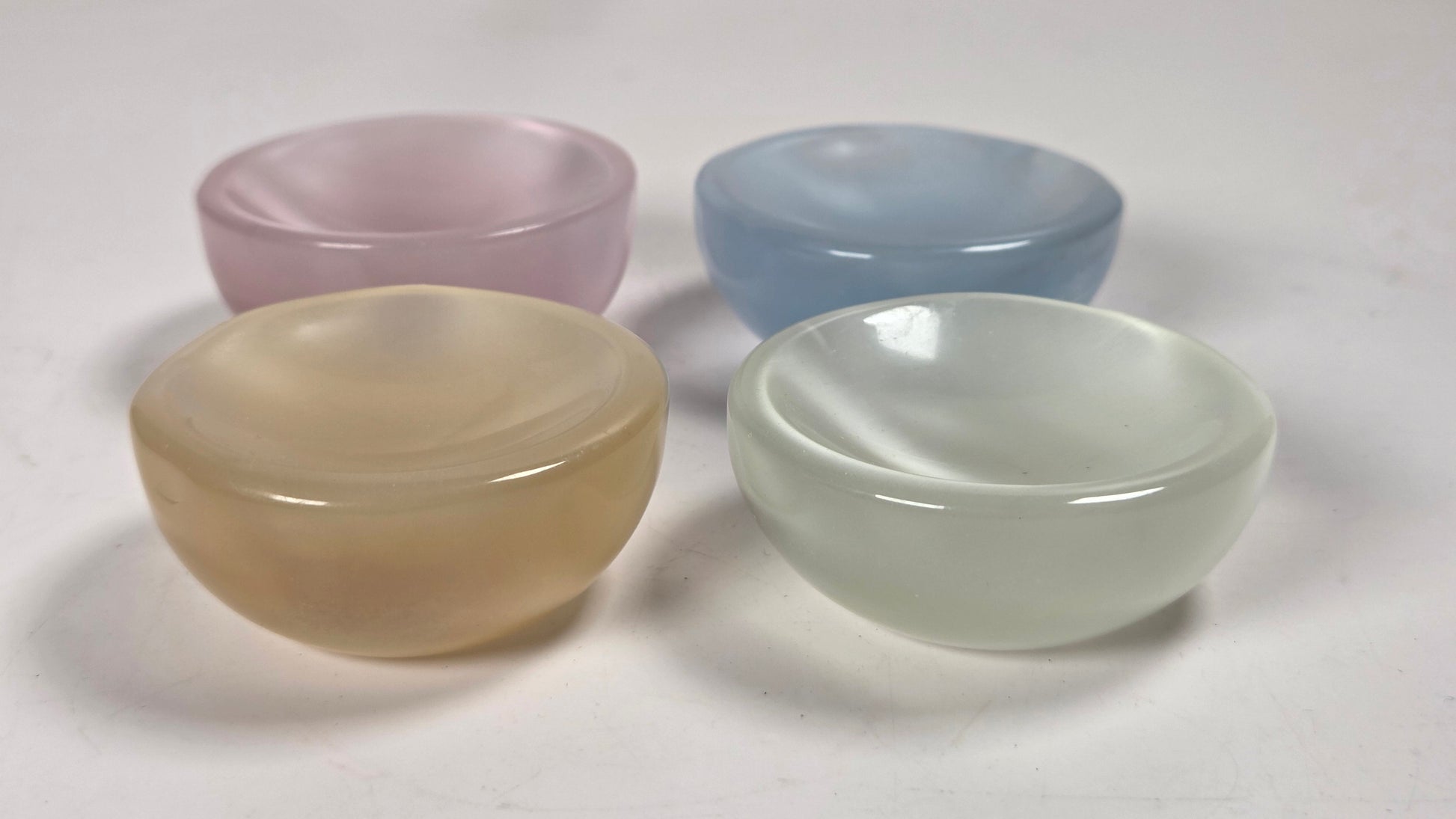 Four small translucent oval bowls in pastel colors, including pink, blue, pale yellow, and mint green, arranged on a light surface.