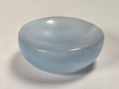 A small, smooth, dome-shaped translucent light blue glass object, possibly a dish, candle holder, or decorative piece, shown on a plain off-white surface.