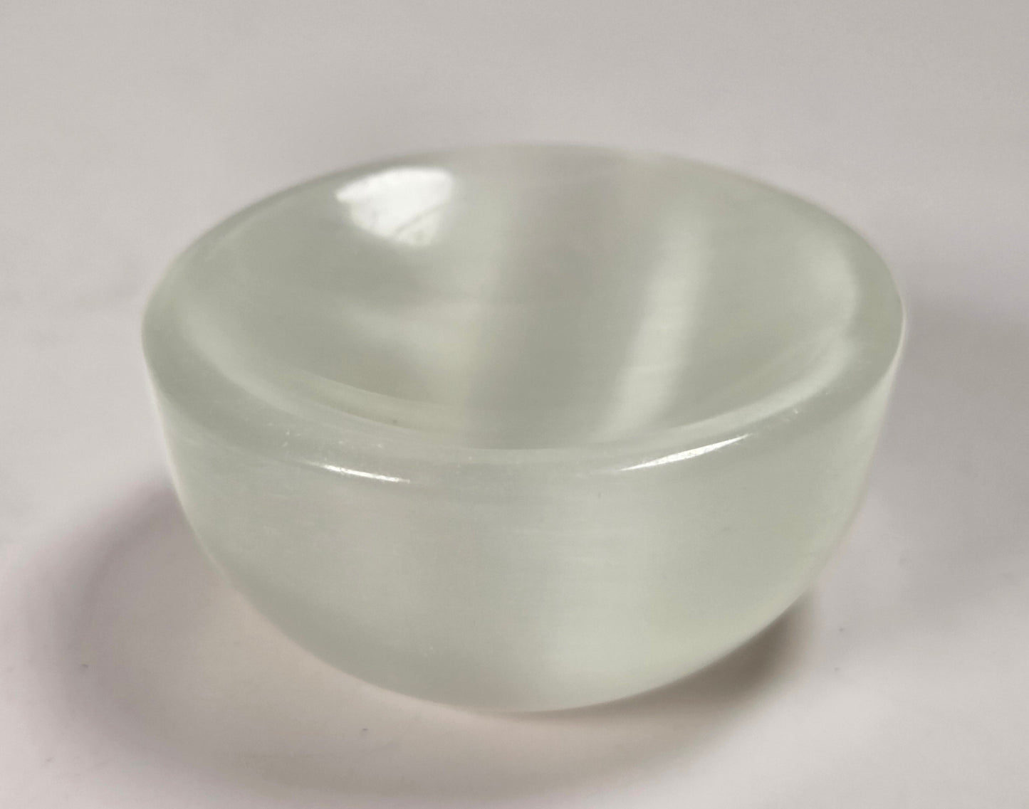 A small, round, translucent white glass bowl with a smooth, glossy finish, set against a plain light gray background.