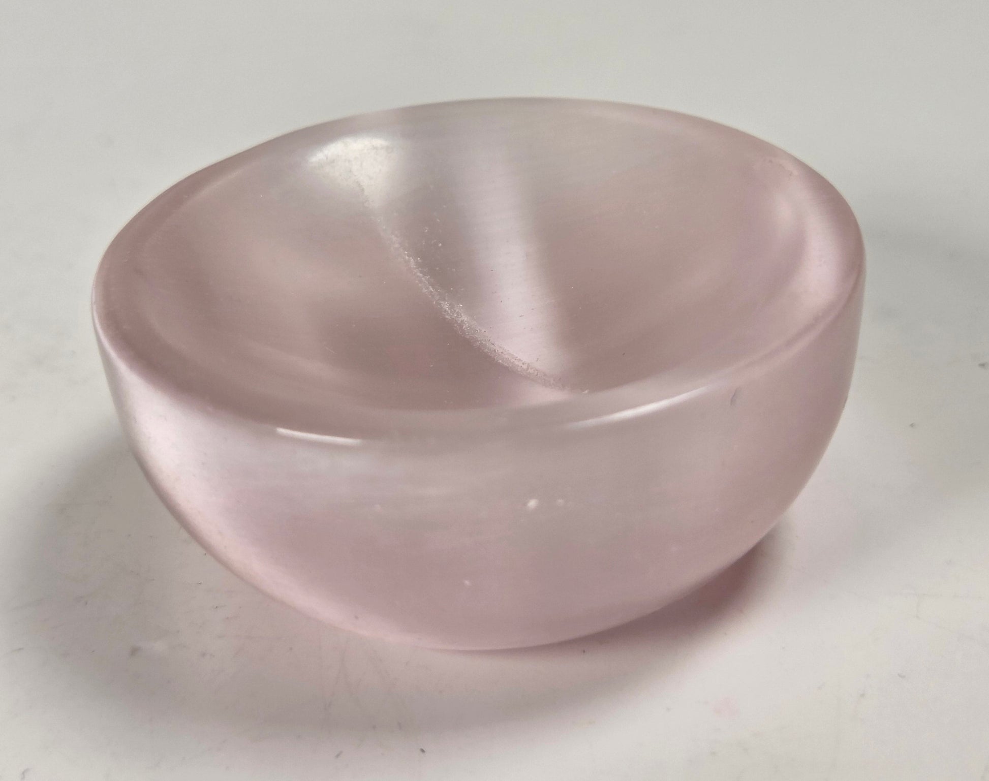 A small, smooth, semi-translucent pink stone bowl, likely rose quartz, photographed on a plain light gray surface.