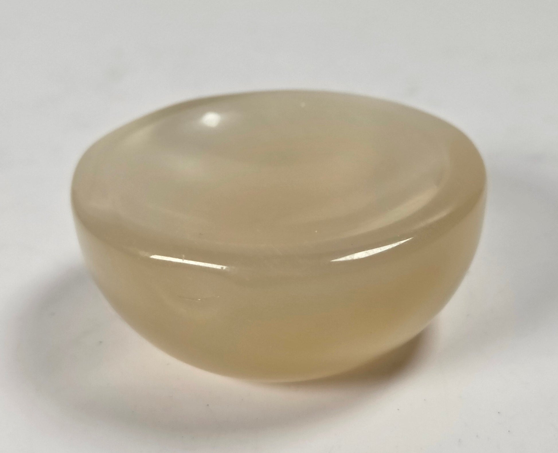 A small, smooth, rounded translucent stone object with a warm beige-tan hue, photographed on a plain light background.