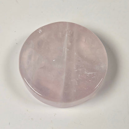 A round, polished pink stone cabochon, likely rose quartz, displayed on a plain off-white surface.