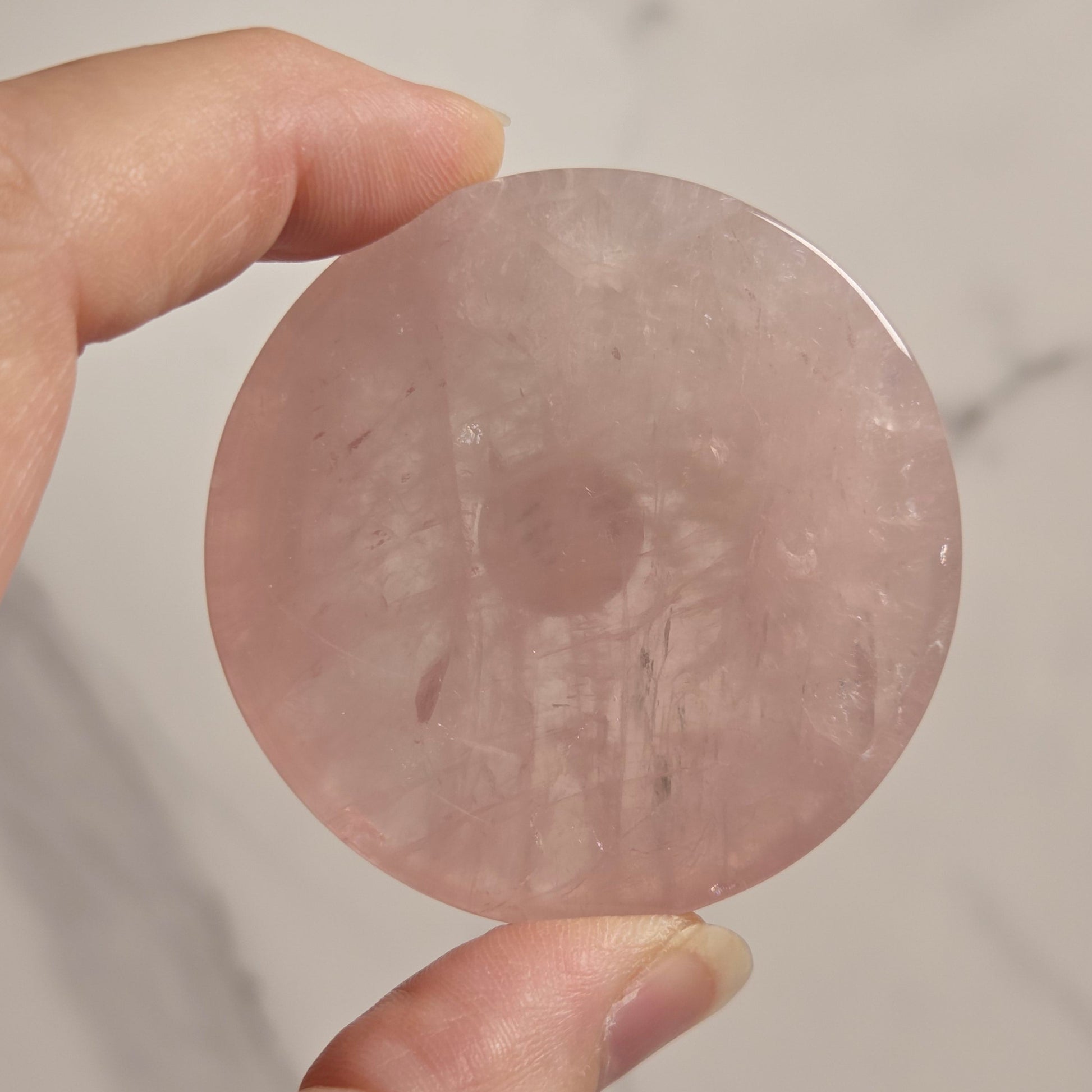 A hand holding a round, flat pink stone disc against a light marble-patterned background.