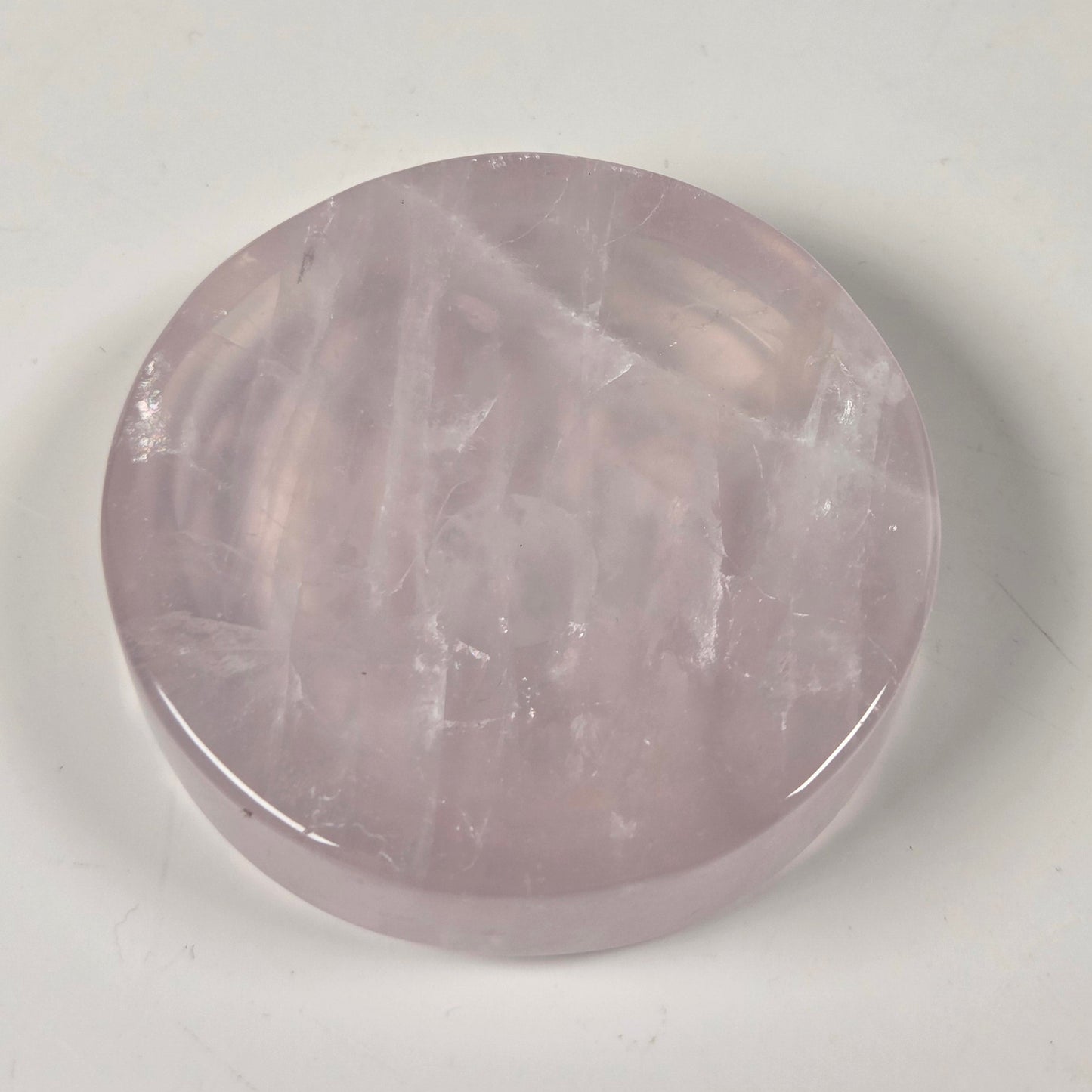A round, polished pink gemstone, likely rose quartz, displayed on a plain off-white surface.