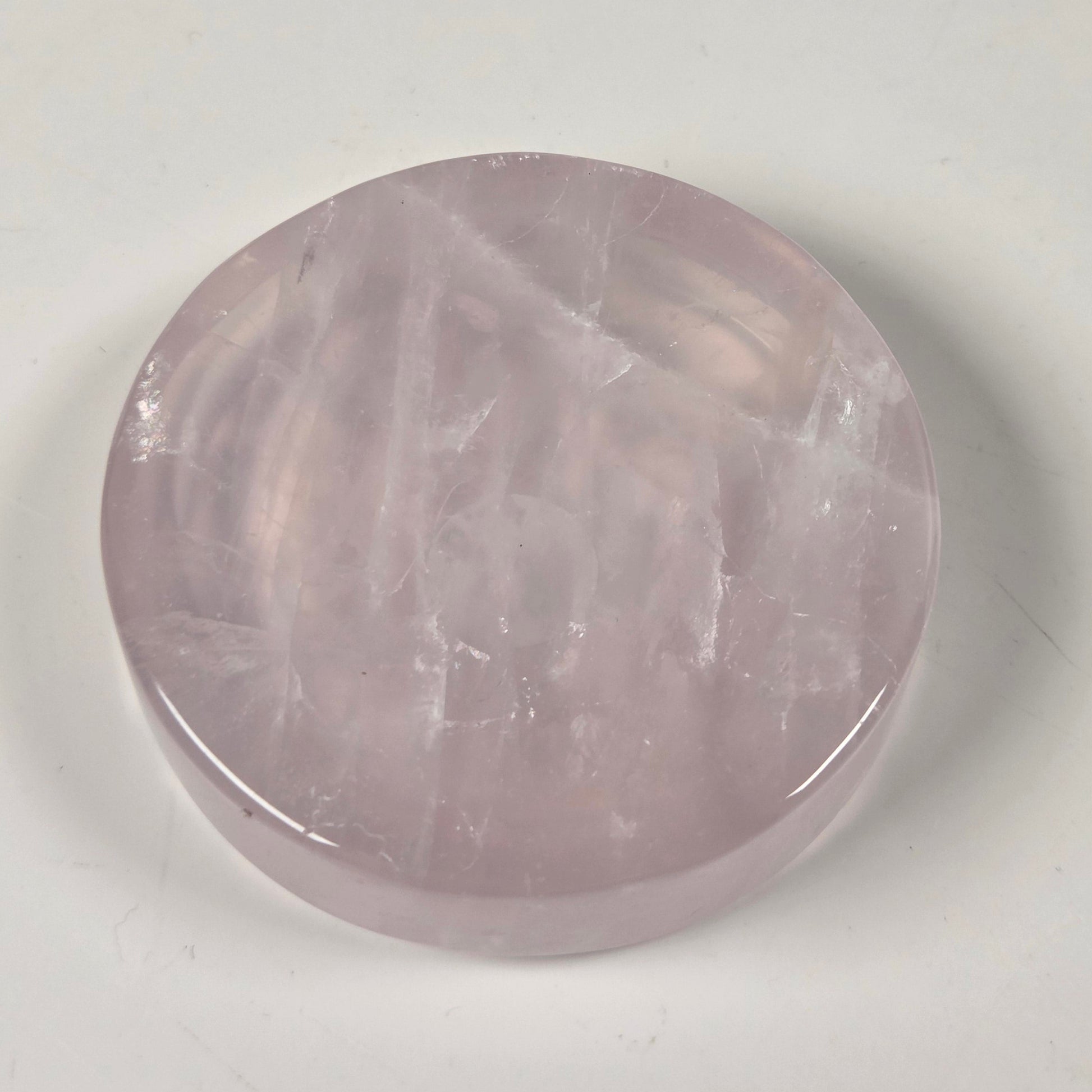 A round, polished pink gemstone, likely rose quartz, displayed on a plain off-white surface.