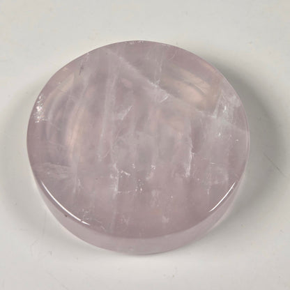 A round, polished pink gemstone, likely rose quartz, displayed on a plain off-white surface.