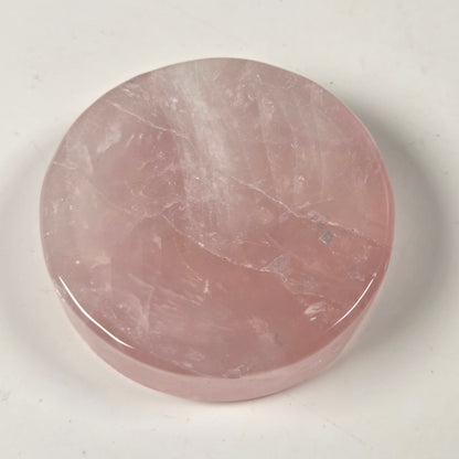 A round, polished pink rose quartz crystal pendant or medallion, displayed on a light off-white background.