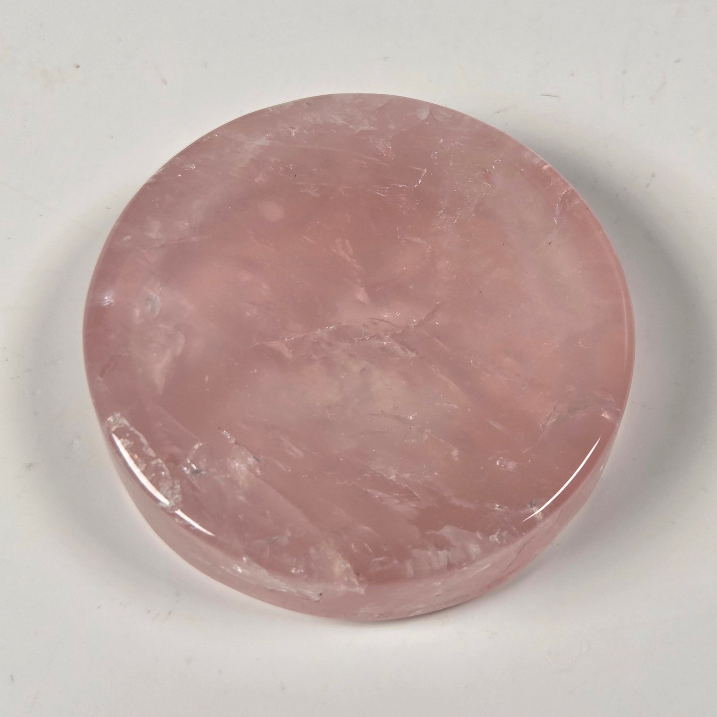 A round, polished pink stone slab, likely rose quartz, displayed on a neutral off-white background.