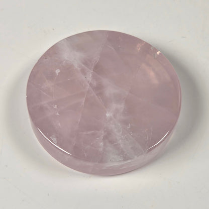 A round, polished pink stone cabochon with natural white veining, displayed on a neutral off-white background.