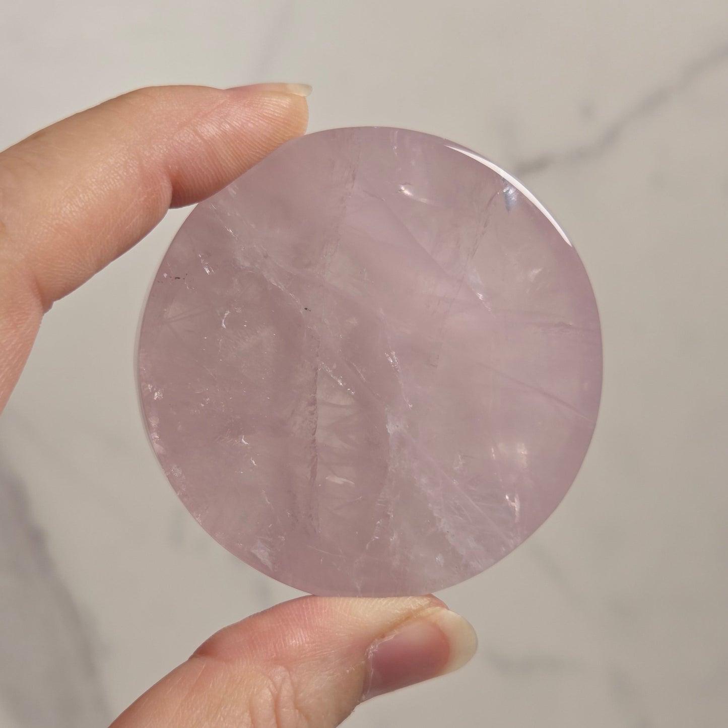 A hand holding a round, polished pink stone or crystal against a light marble-like background.