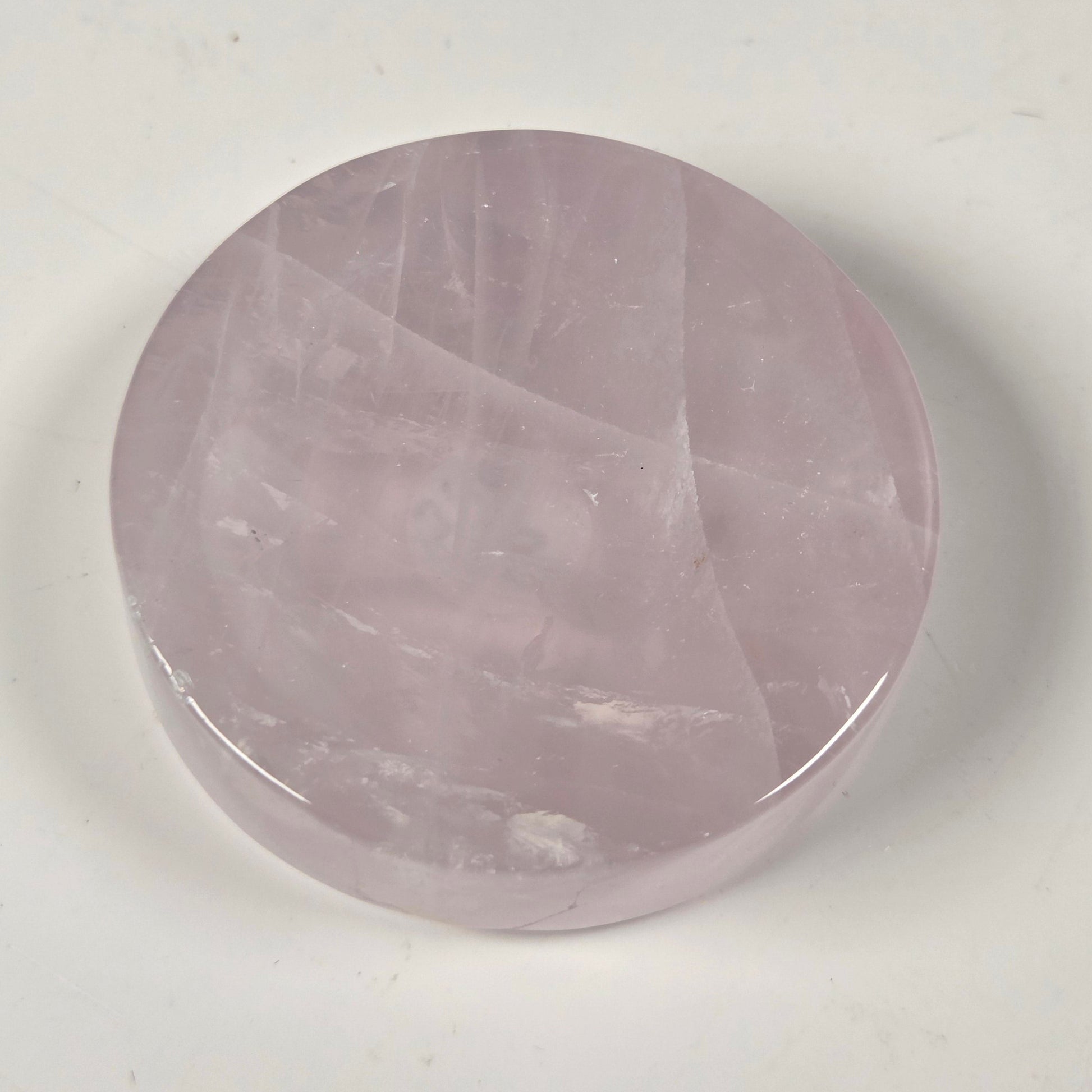 A round, polished pink stone cabochon, likely rose quartz, displayed on a plain off-white surface.