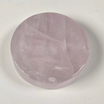 A round, polished pink stone cabochon, likely rose quartz, displayed on a plain off-white surface.