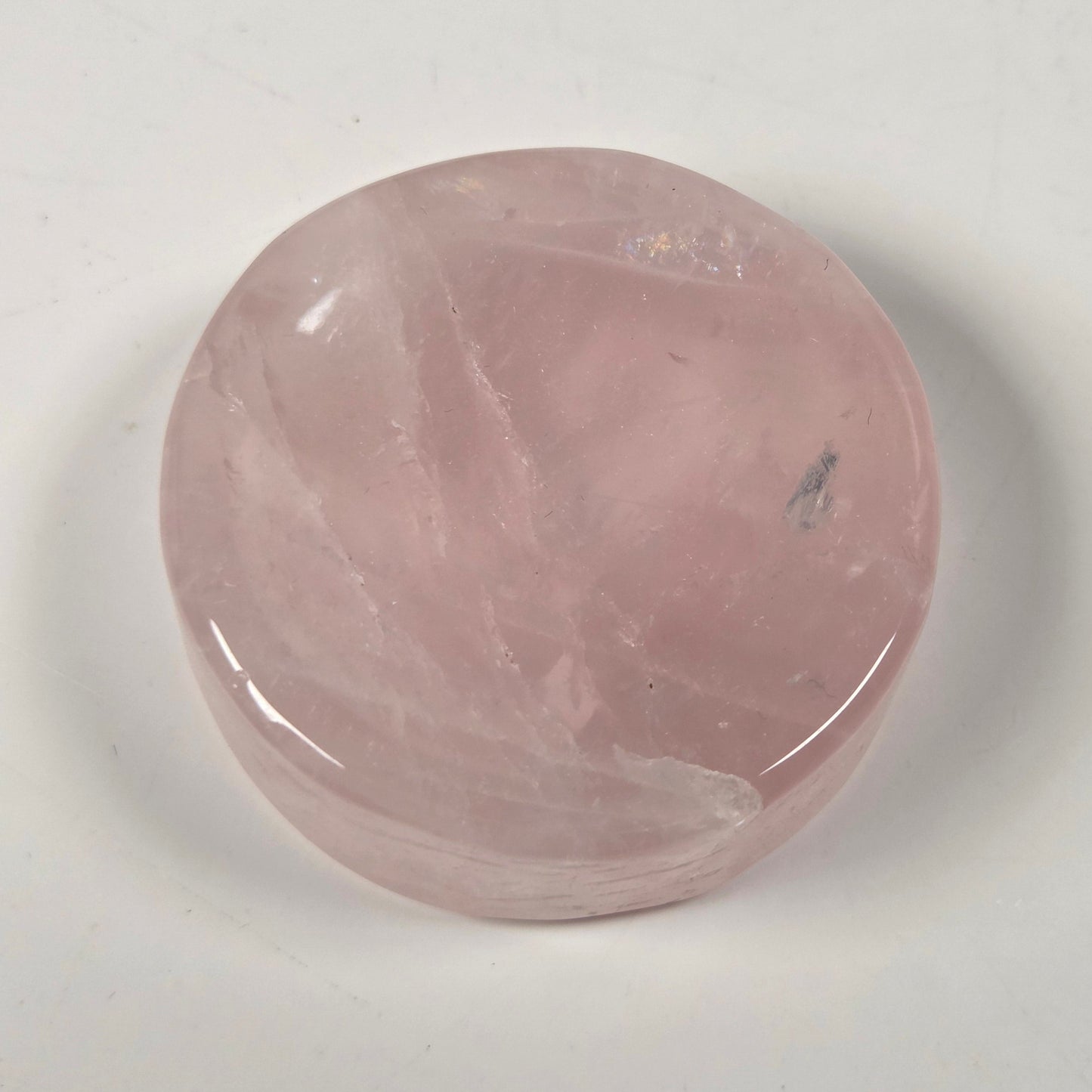 A polished pink rose quartz cabochon stone with natural internal veining, resting on a plain off-white surface.