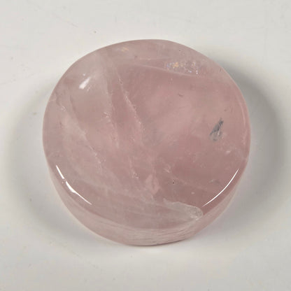 A polished pink rose quartz cabochon stone with natural internal veining, resting on a plain off-white surface.