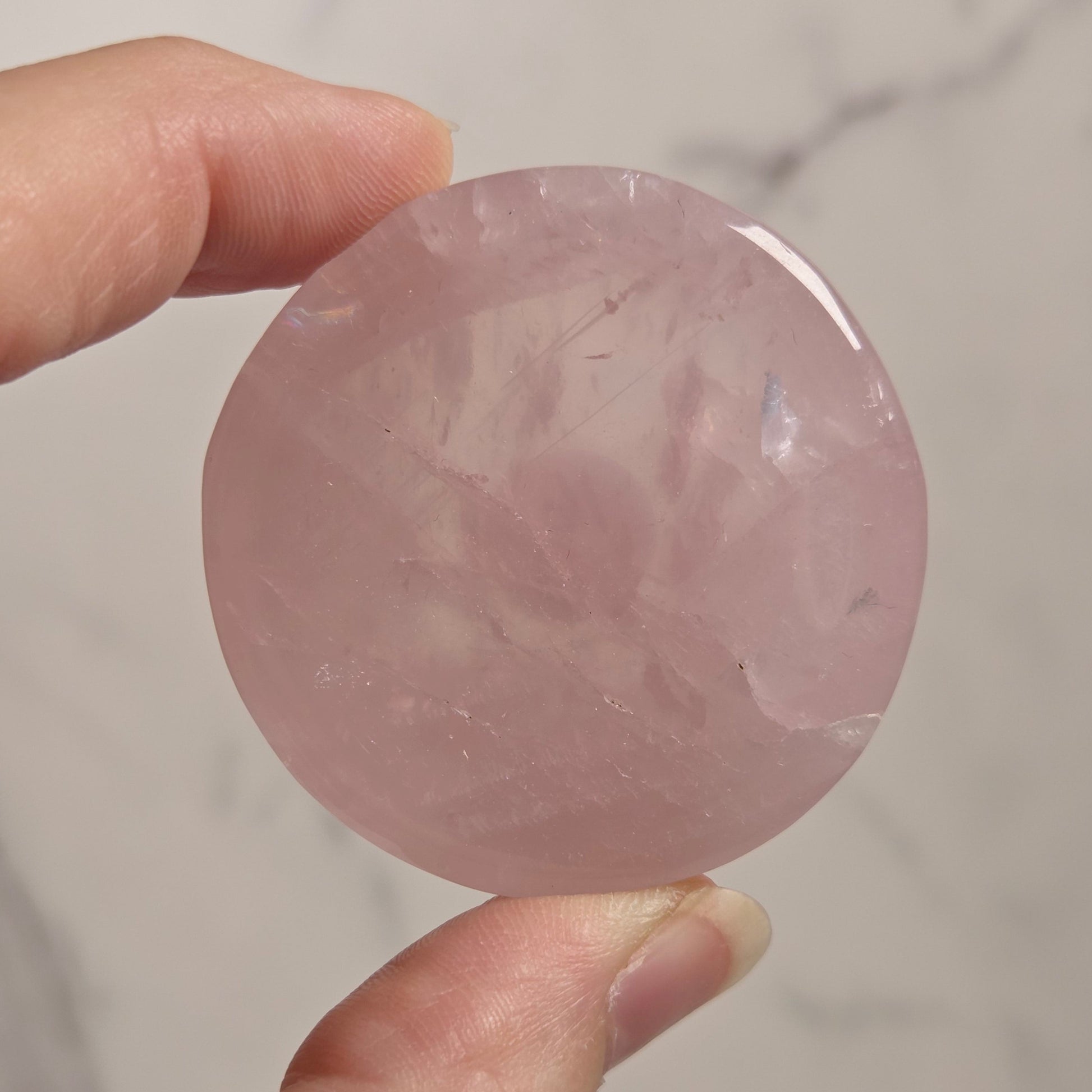 A hand holding a round, polished pink stone or crystal against a light marble-like background.