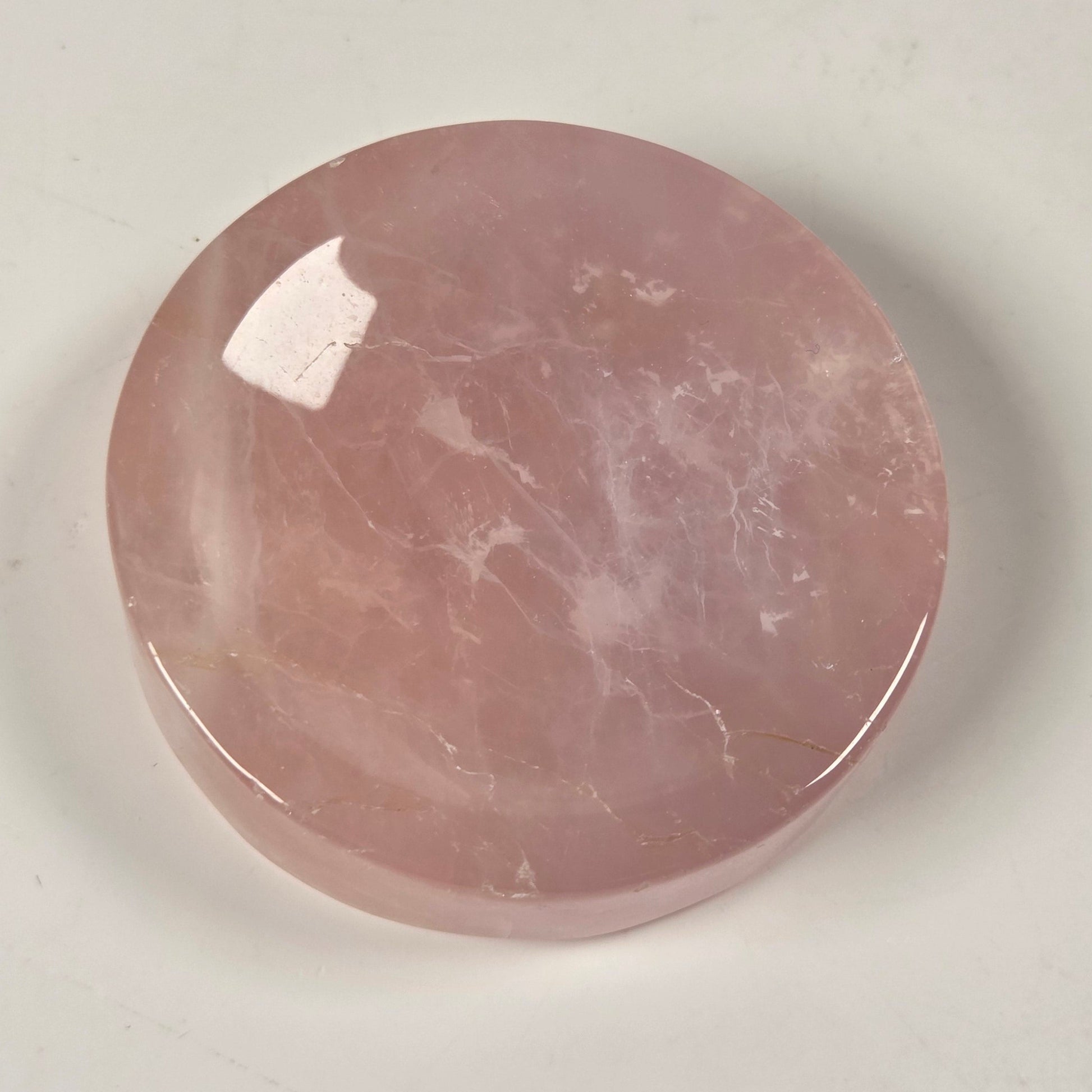 A round, polished pink stone cabochon with natural white veining, displayed on a light off-white background.