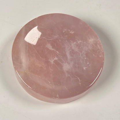 A round, polished pink stone cabochon with natural white veining, displayed on a light off-white background.