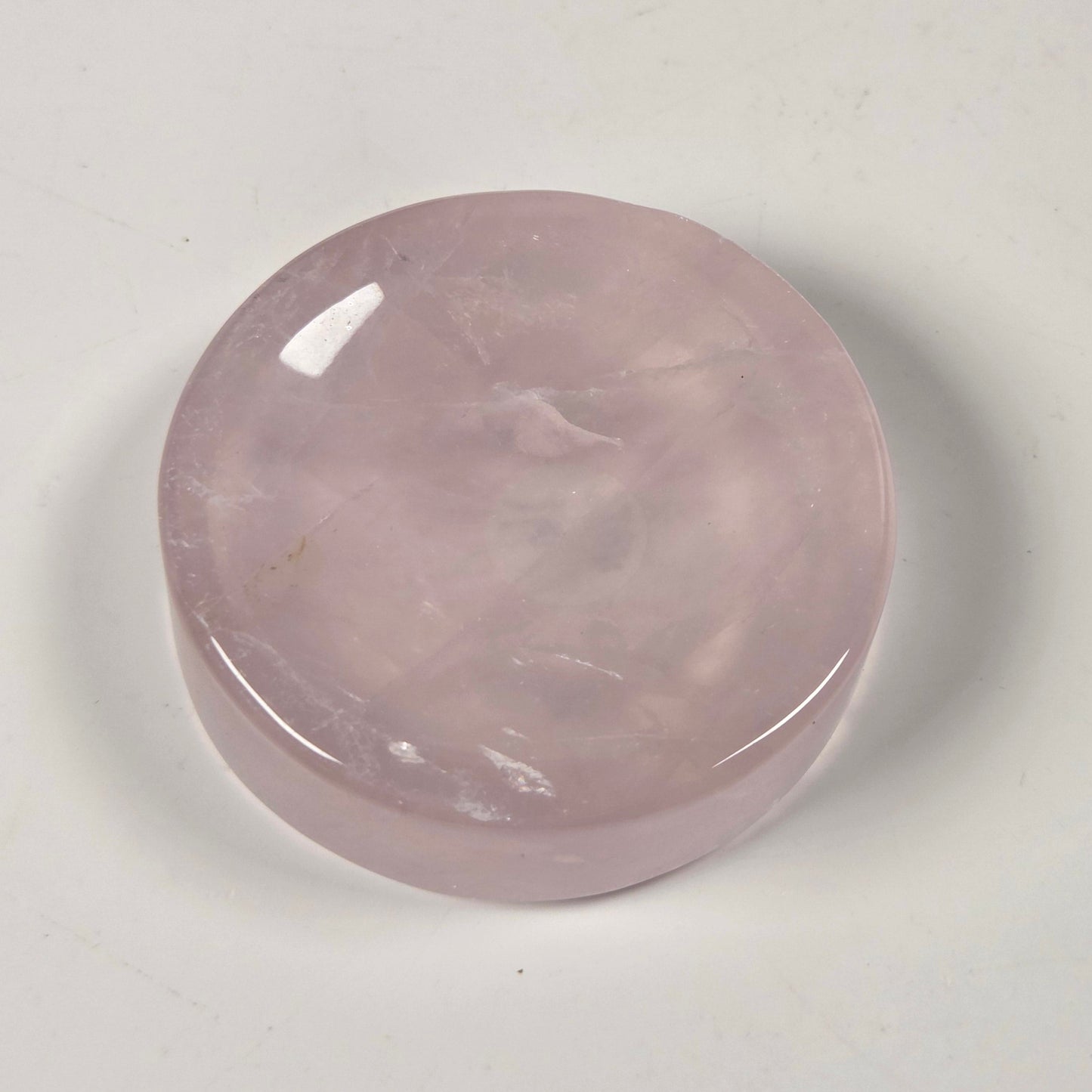 A polished, round rose quartz crystal cabochon with a smooth, glossy finish, resting on a plain off-white surface.