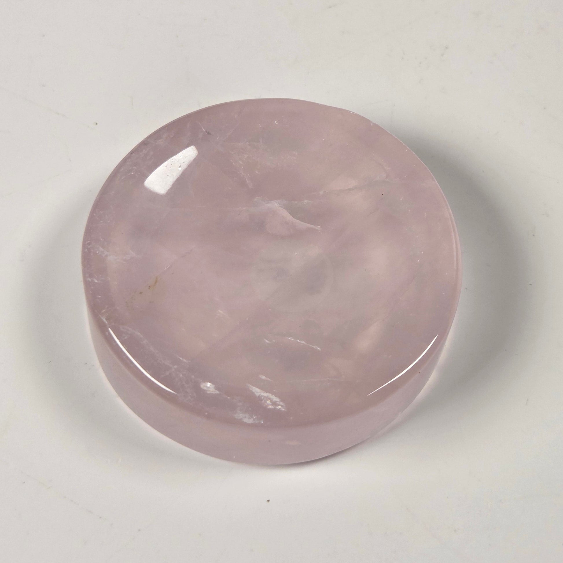 A polished, round rose quartz crystal cabochon with a smooth, glossy finish, resting on a plain off-white surface.