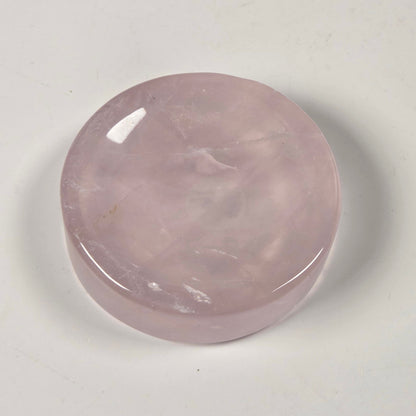 A polished, round rose quartz crystal cabochon with a smooth, glossy finish, resting on a plain off-white surface.