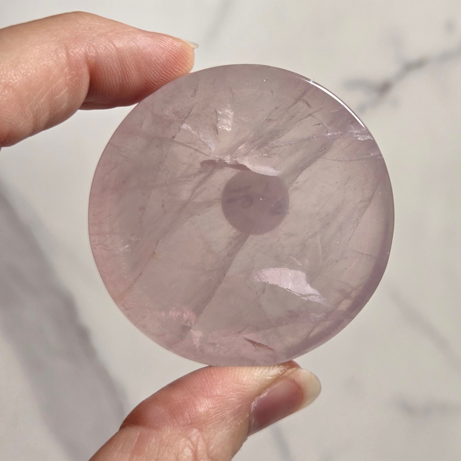 A hand holding a round, polished pink stone disc against a light marble-patterned background.