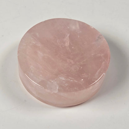 A round, polished pink stone object, likely a rose quartz decorative piece or coaster, photographed on a plain light gray background.