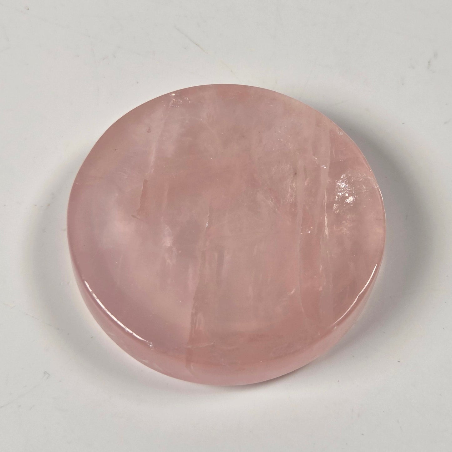 A round, polished pink stone cabochon with natural inclusions, displayed on a neutral light gray background.