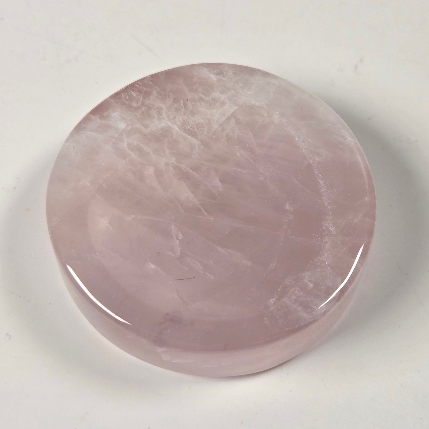 A polished, round rose quartz crystal cabochon with a smooth, glossy finish, resting on a plain off-white surface.