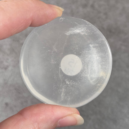 A hand holding a round, semi-transparent clear plastic cap or cover against a textured gray background.