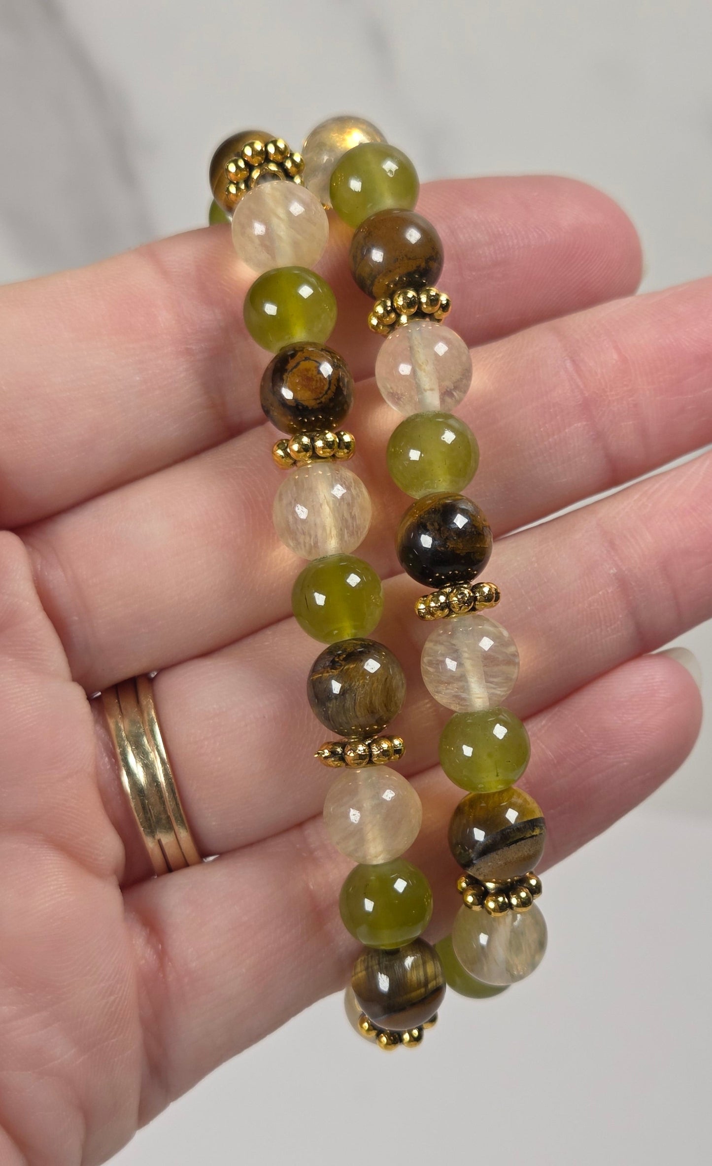 Two beaded stretch bracelets with green, brown, and clear beads separated by gold spacer beads, held in a person's hand.