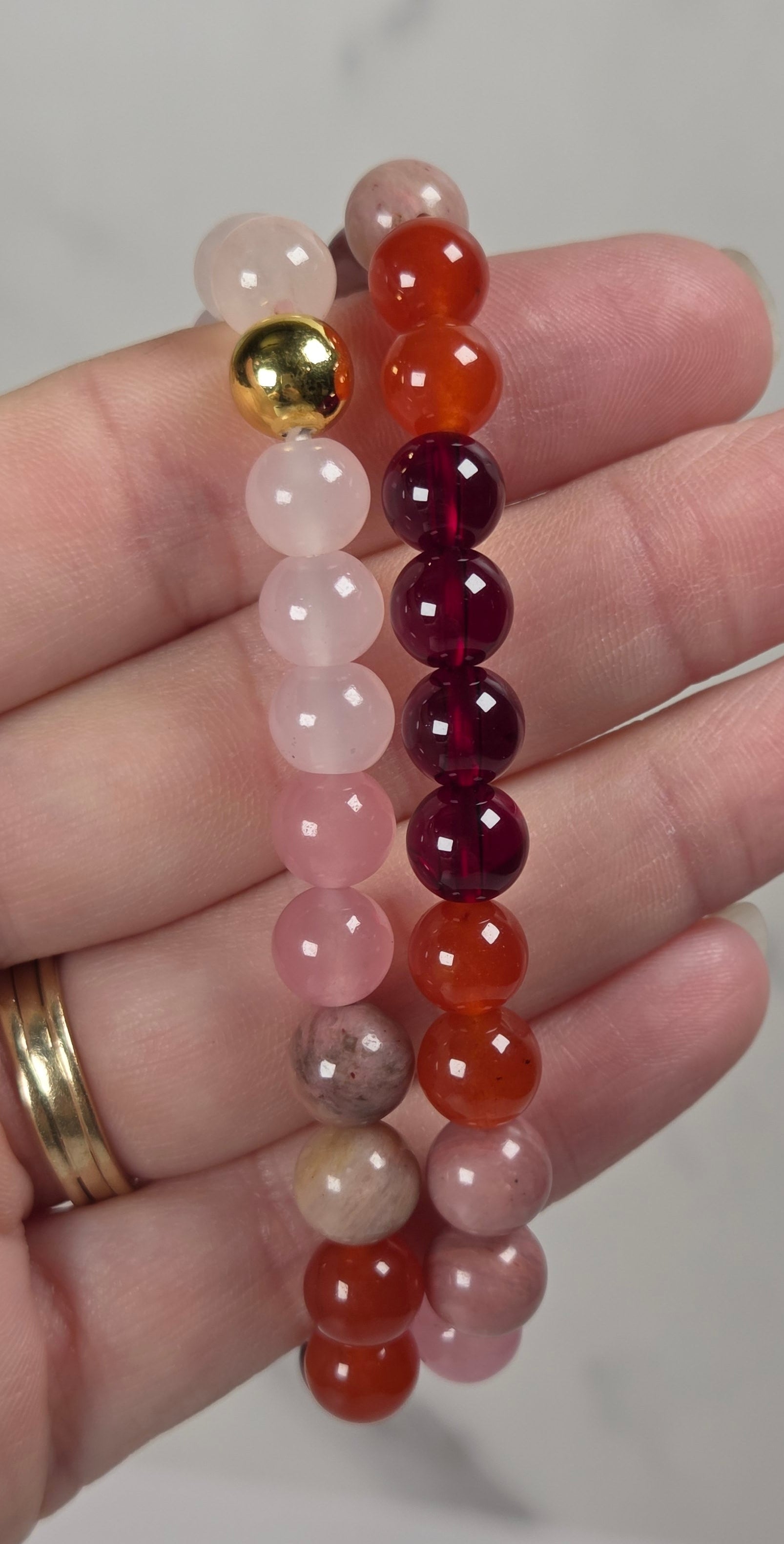 Two beaded stretch bracelets held in a hand. One bracelet features pale pink, peach, and light brown translucent beads with a single gold bead accent.