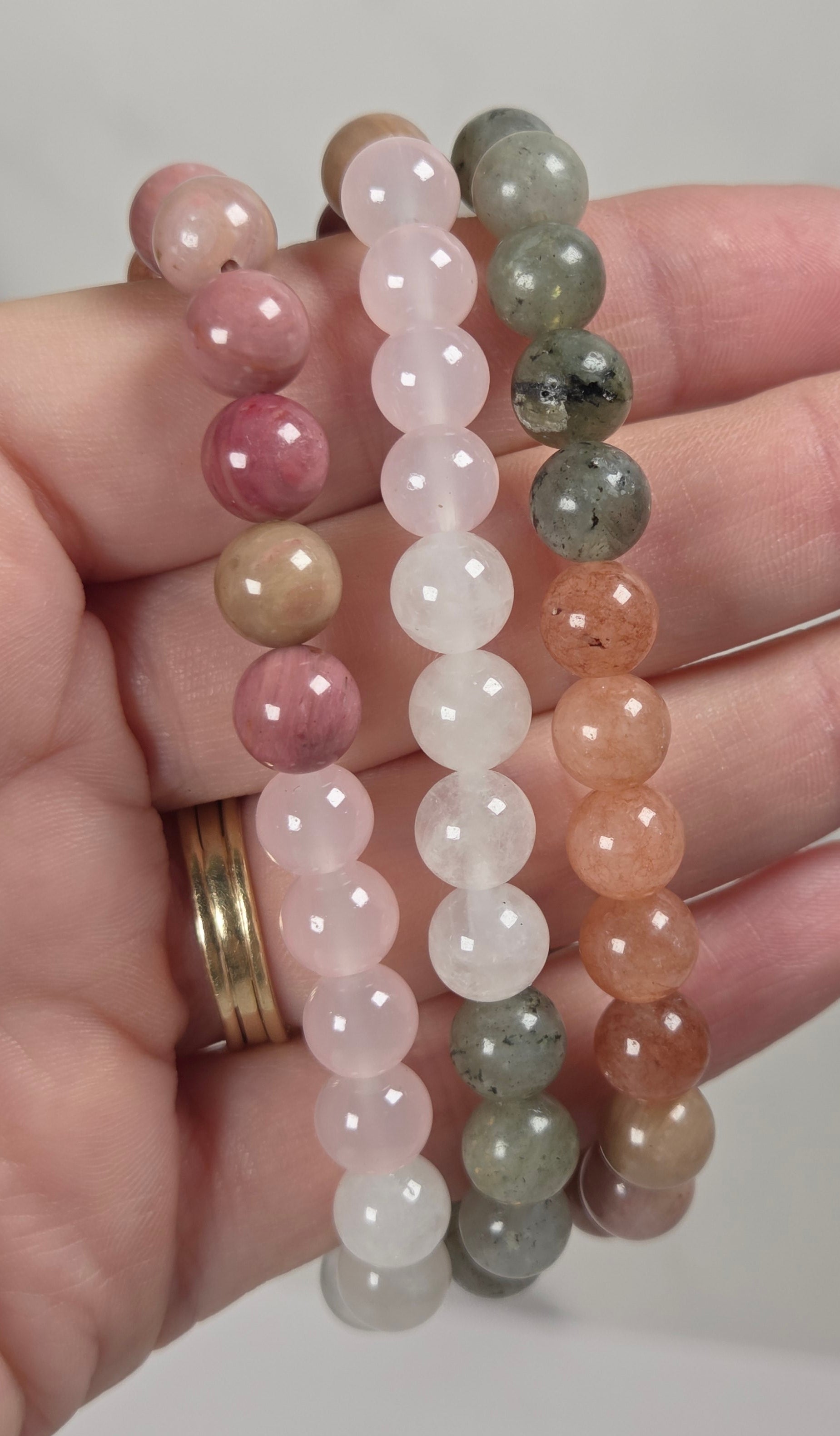 3 beaded bracelets with various color beads being held by a hand against a white background
