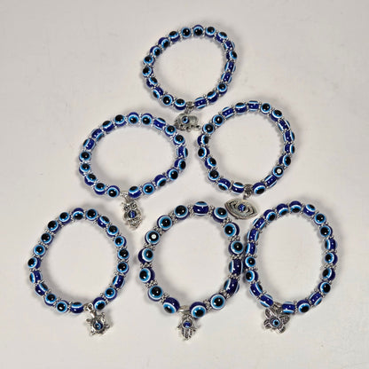 Five blue and black evil eye beaded bracelets with silver charms, arranged in a pyramid on a plain off-white background.
