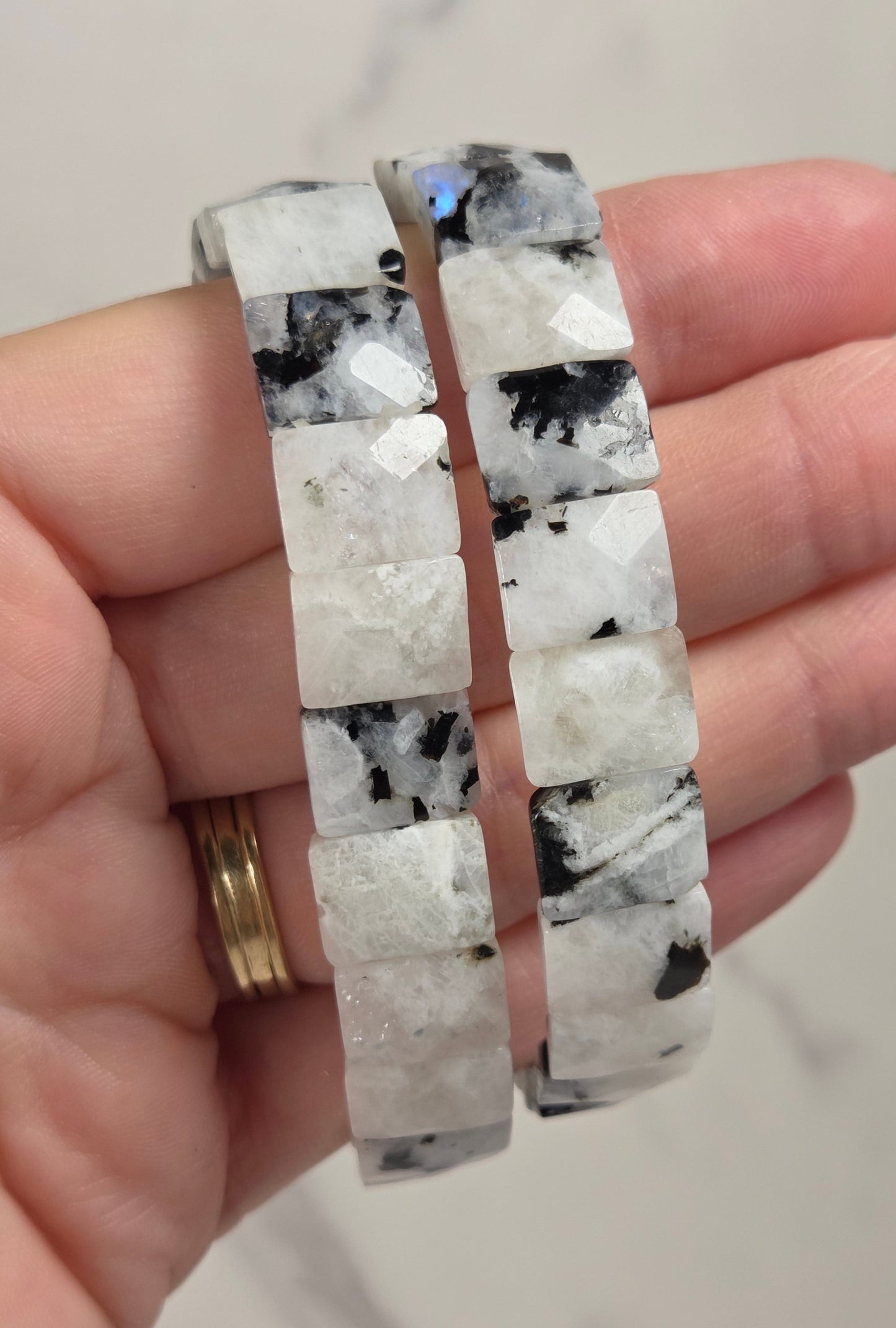 Two chunky beaded bracelets made of white and black marbled stone, held in a person's hand against a light marble background.