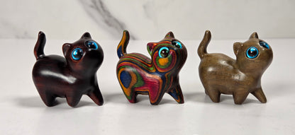 Three small carved cat figurines with large blue eyes, displayed side by side on a light marble surface against a white marble background.