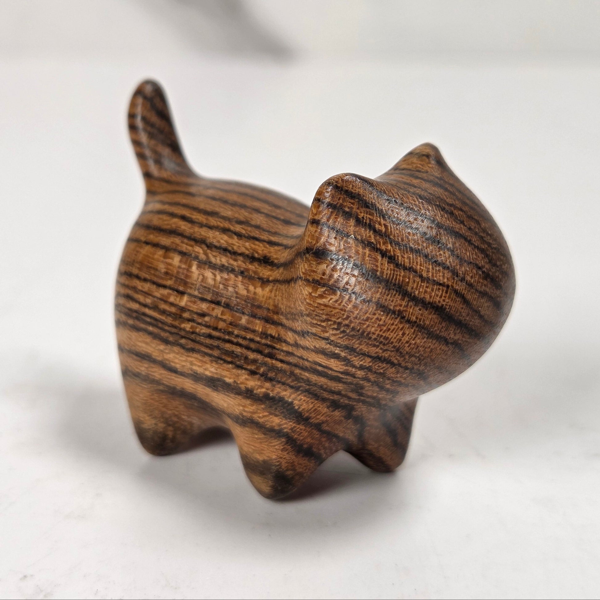 A small carved wooden cat figurine with dark and light brown wood grain, standing on a light gray marble-like surface.