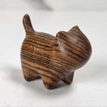 A small carved wooden cat figurine with dark and light brown wood grain, standing on a light gray marble-like surface.