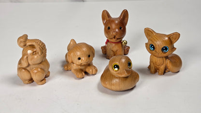 Five small hand-carved wooden animal figurines, including an elephant, puppy, rabbit, duck, and fox, displayed on a white surface with a marble-patterned background.