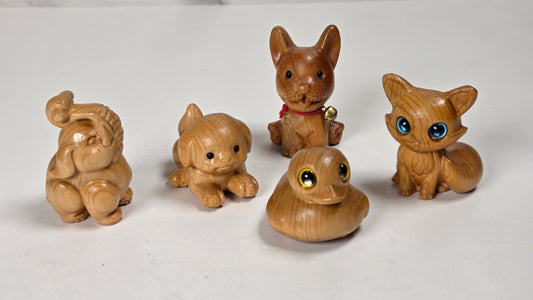 Five small hand-carved wooden animal figurines, including an elephant, puppy, rabbit, duck, and fox, displayed on a white surface with a marble-patterned background.