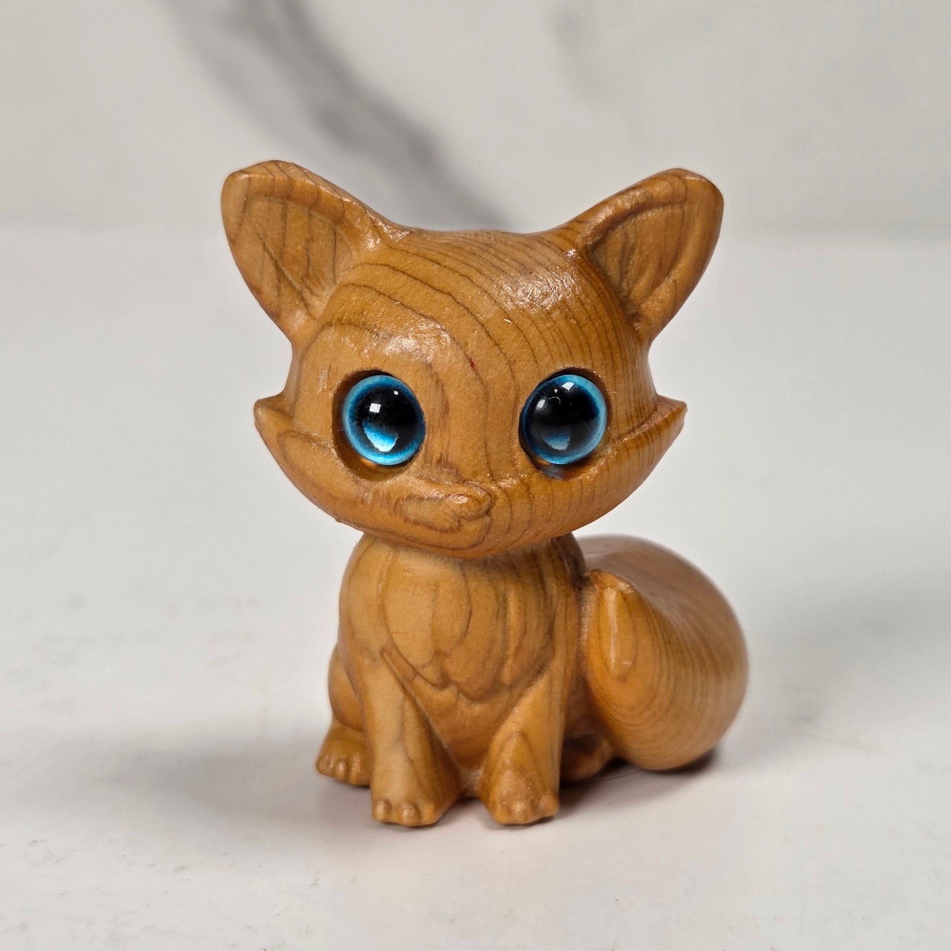 A small wooden fox figurine with large, glossy blue eyes, sitting on a light gray marble-like surface.
