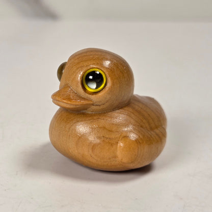A small wooden duck figurine with a glossy finish and realistic yellow-rimmed eyes, standing on a light off-white surface.