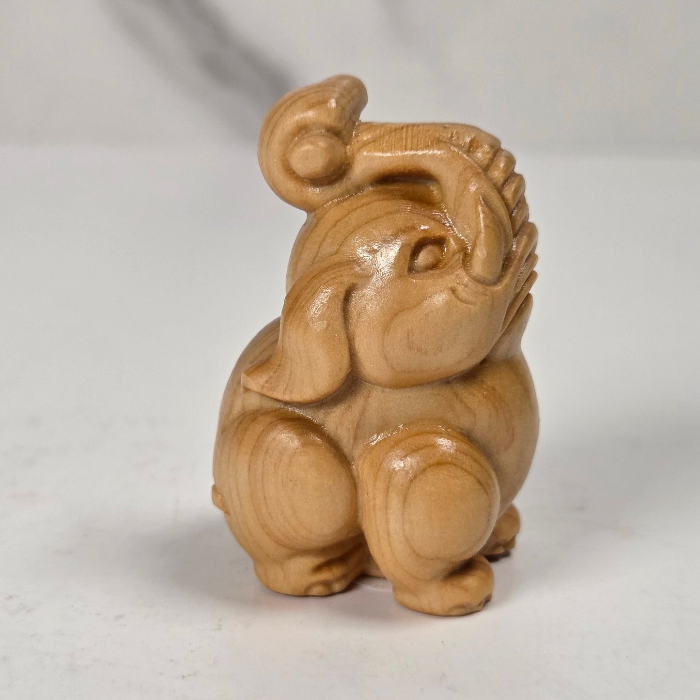 A small carved wooden elephant figurine with a glossy finish, sitting on a light gray surface against a white marble-patterned background.