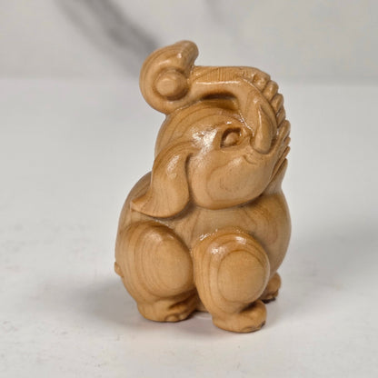A small carved wooden elephant figurine with a glossy finish, sitting on a light gray surface against a white marble-patterned background.