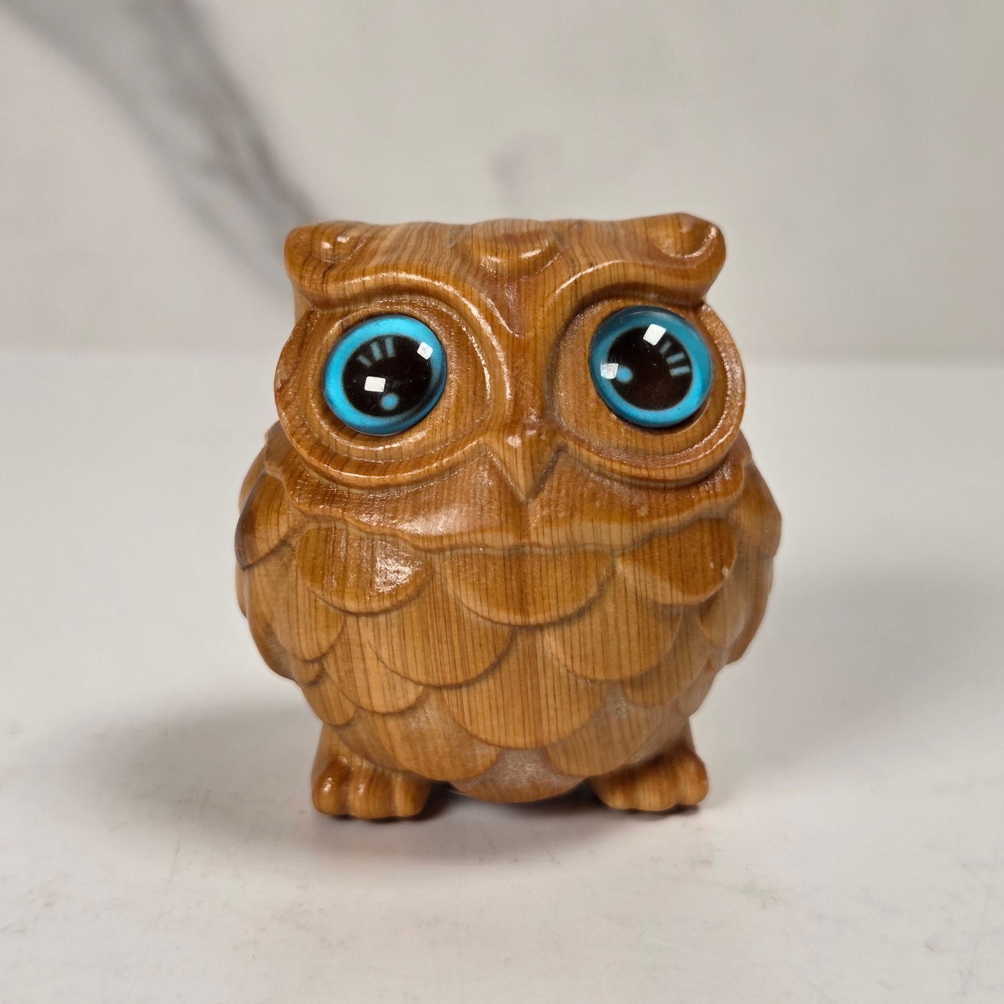 A small carved wooden owl figurine with large, glossy blue and black eyes, standing on a light surface against a neutral background.