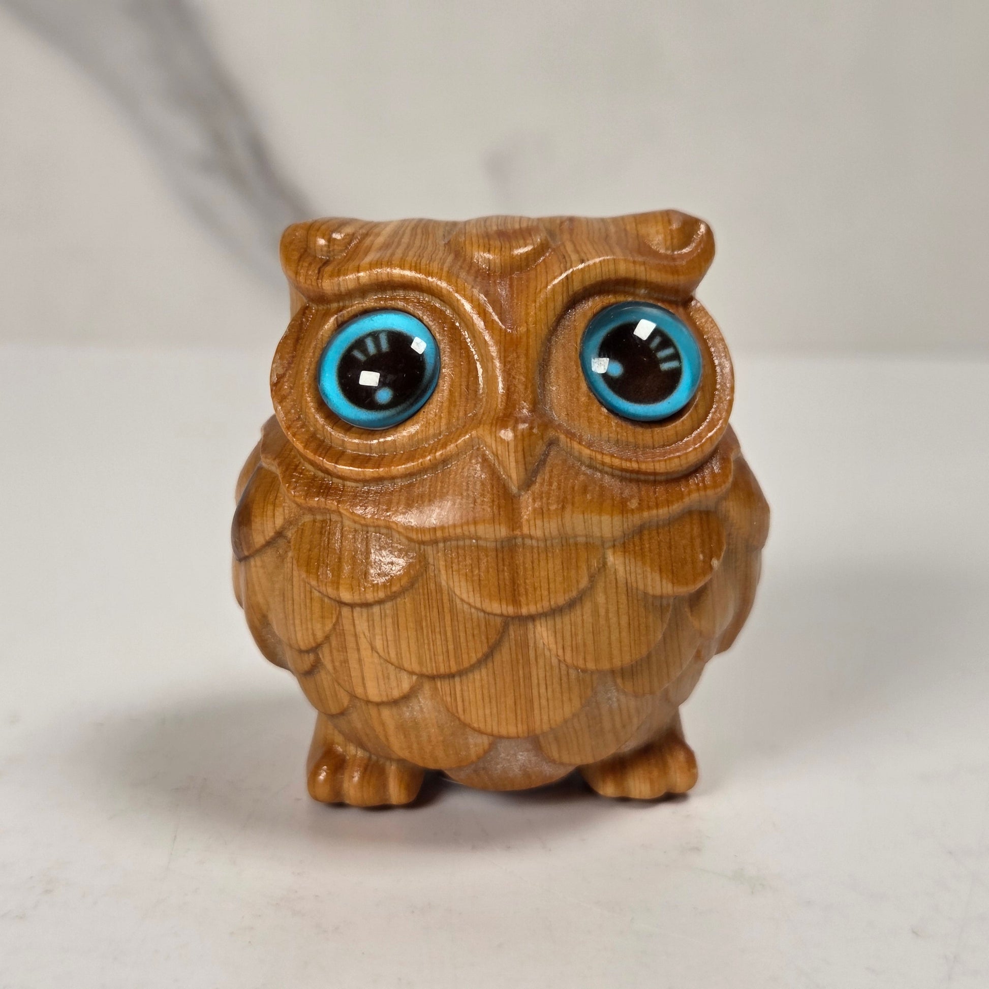 A small carved wooden owl figurine with large, glossy blue and black eyes, standing on a light surface against a neutral background.