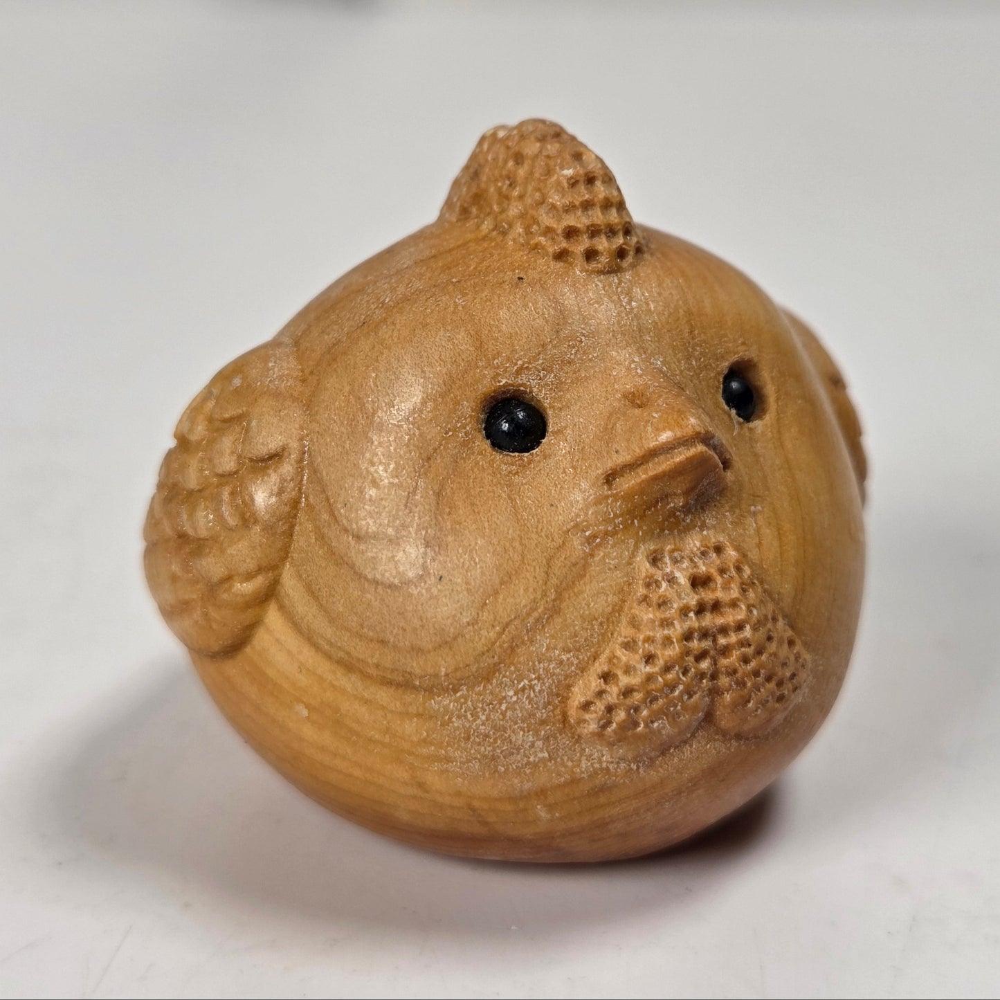 A small carved wooden bird figurine with black bead eyes and a beak, shown on a plain light background.