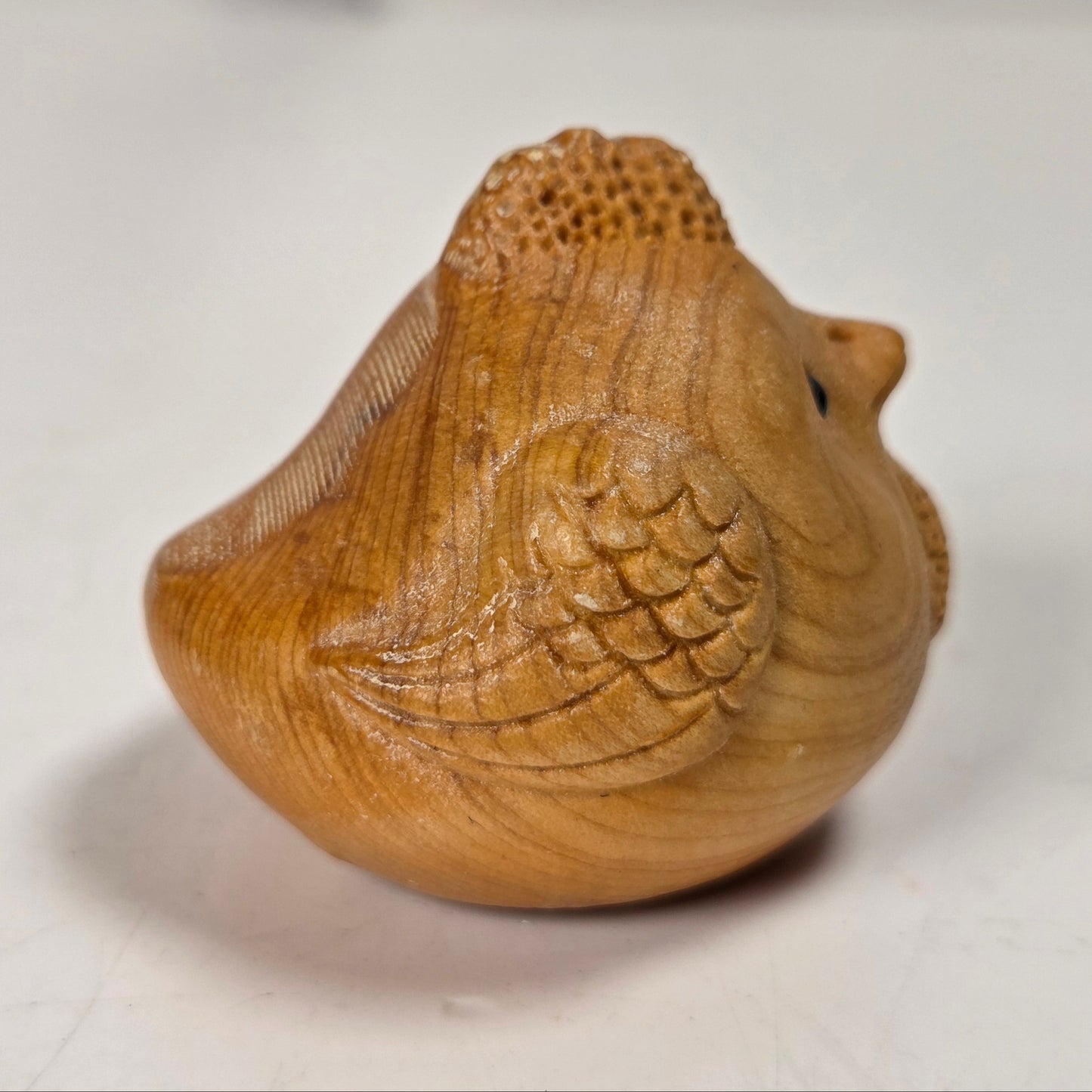 A small carved wooden bird figurine with detailed feather and beak carvings, shown on a light gray surface.
