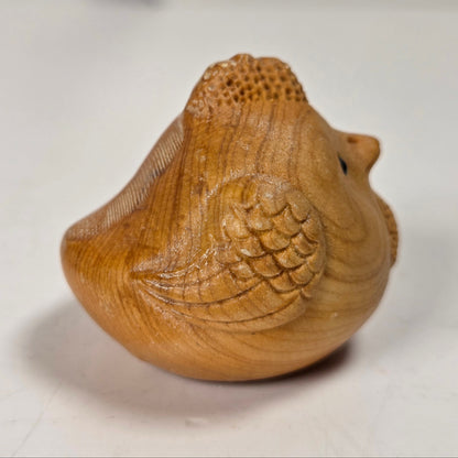 A small carved wooden bird figurine with detailed feather and beak carvings, shown on a light gray surface.