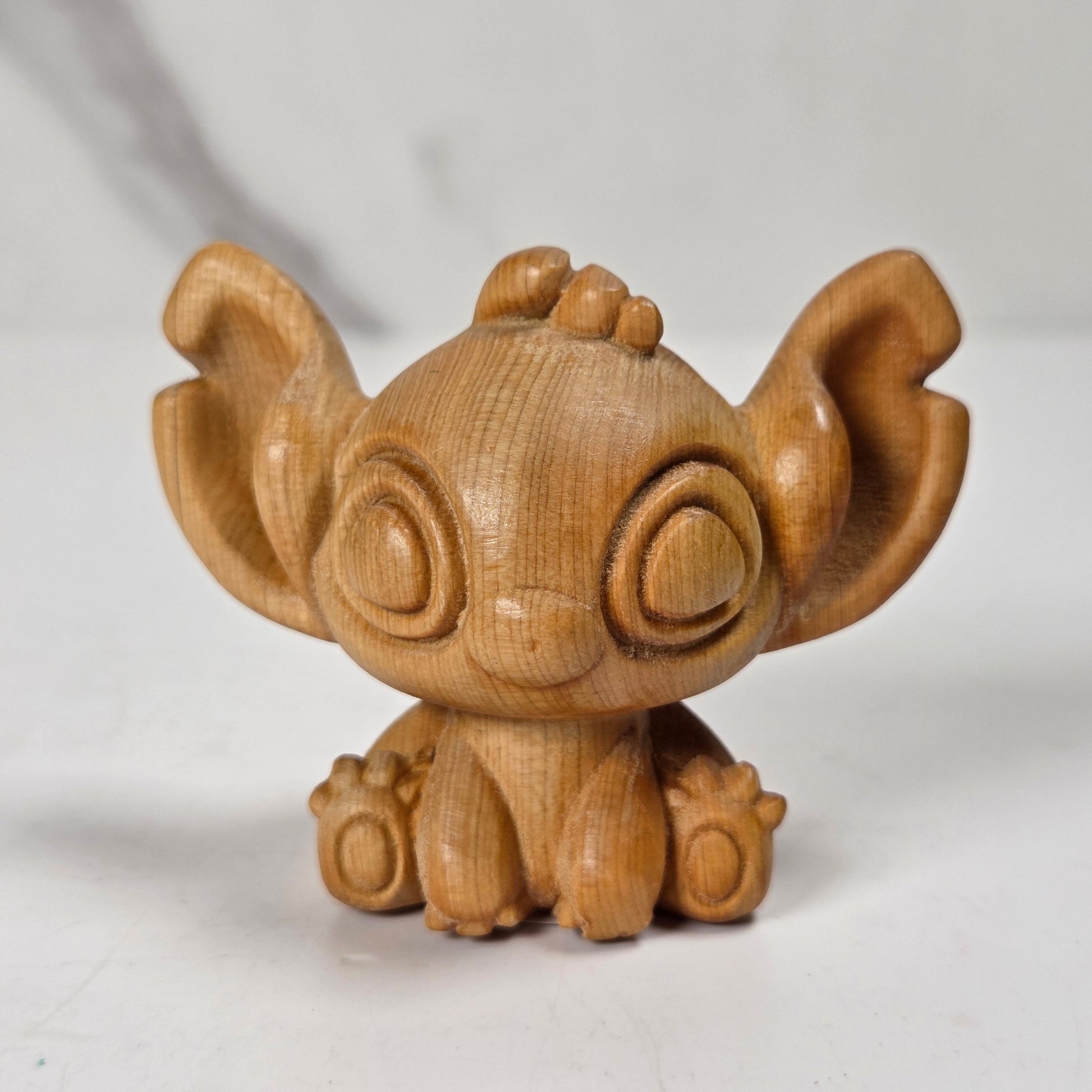 A small wooden figurine of a cartoon character with large ears and round eyes, shown on a plain light background.